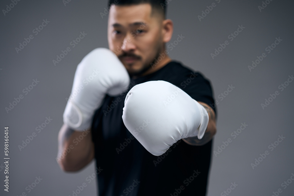 Portrait of asian young man in black t shirt hitting at camera in white boxing gloves