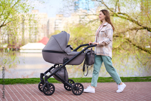 Fényképezés Portrait of beautiful smiling young mother pushing stroller with little baby walking in spring park