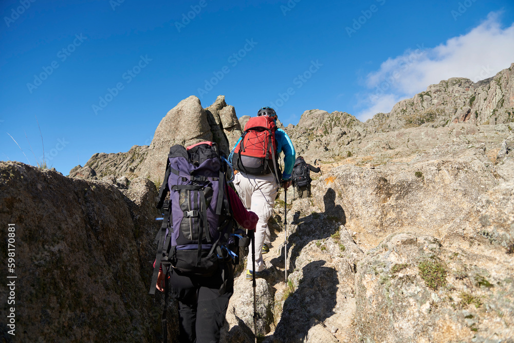 Unrecognizable mountaineers hiking up a trail amidst a rocky mountain landscape in Los Gigantes, Cordoba, Argentina, an ideal tourist destination for trekking and climbing.