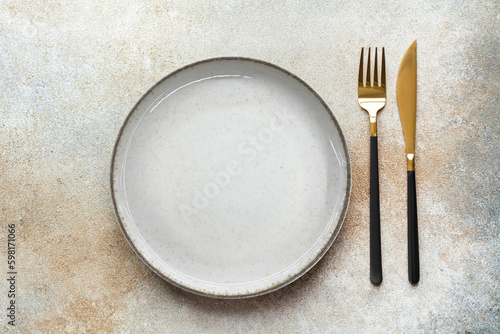 Empty beige plate, knife and fork on a brown background. Cutlery, top view.