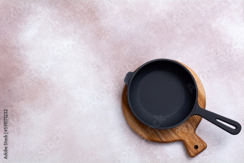 Cast iron skillet on a wooden cutting board on light background. Kitchen utensils. Empty place. Top view.