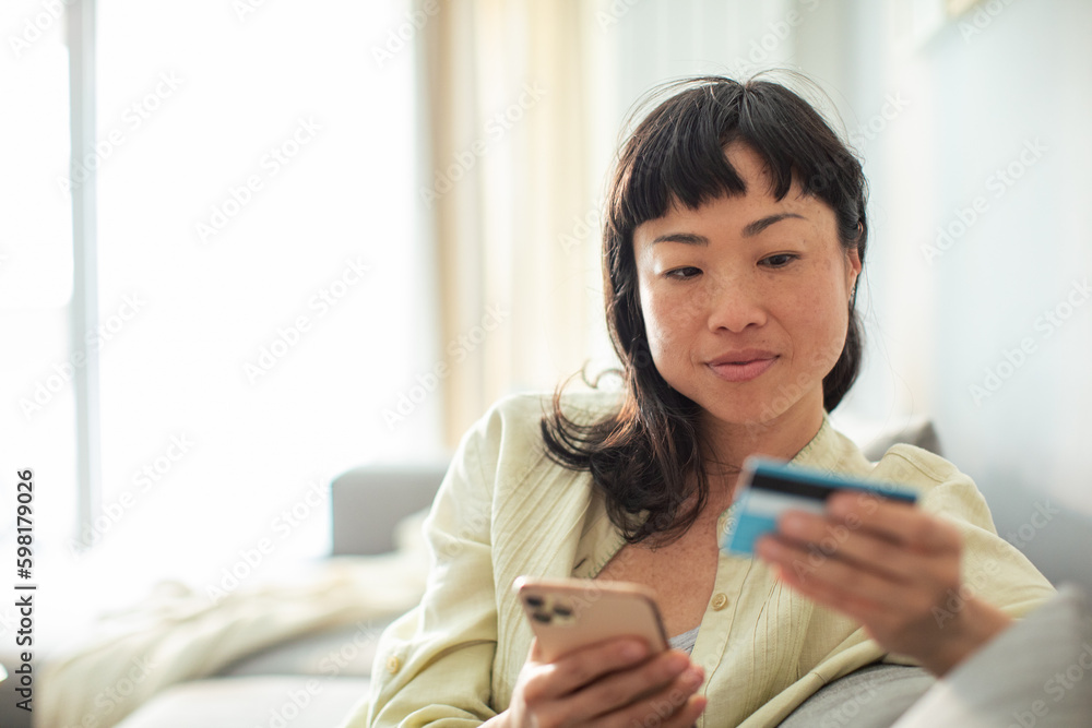 Young Japanese woman online shopping on her smart phone from the comfort of her couch Young Japanese woman online shopping on her smart phone from the comfort of her couch