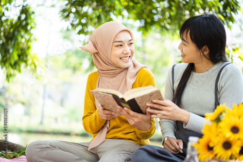 Happy beautiful Asian females Muslim student and friends reading a textbook together in a park. Diversity in ethnic and religious concept.
