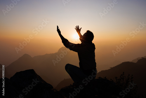 Silhouette of a man is praying to God on the mountain. Praying hands with faith in religion and belief in God on blessing background. Power of hope or love and devotion.