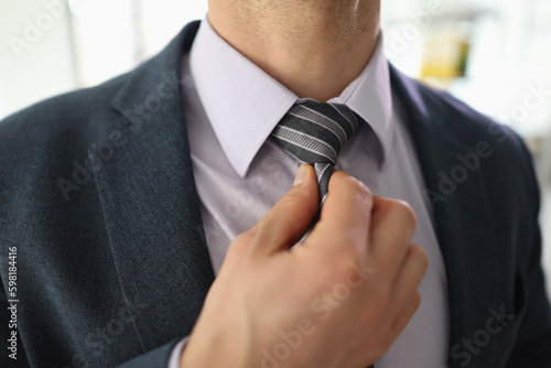 Successful businessman adjusts striped tie with hand