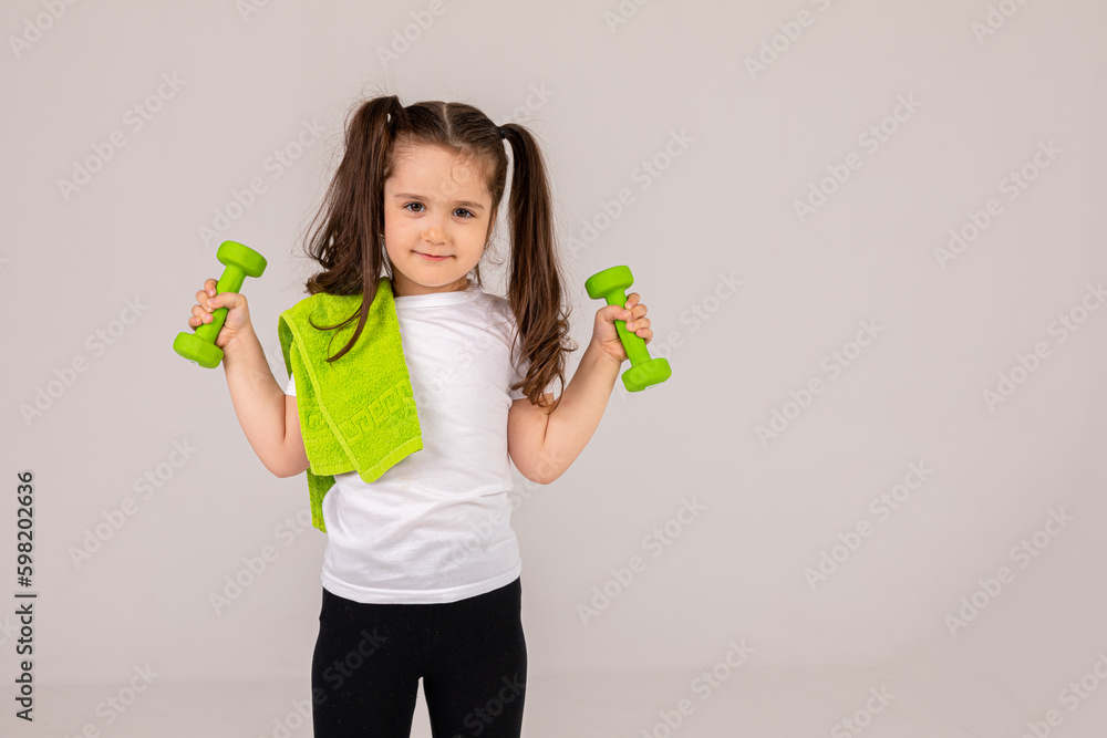 Little child girl with a dumbbells in her hand on a white background. The child leads a healthy lifestyle and goes in for sports. advertising for a gym or fitness club Little child girl with a dumbbells in her hand on a white background. The child leads a healthy lifestyle and goes in for sports. advertising for a gym or fitness club