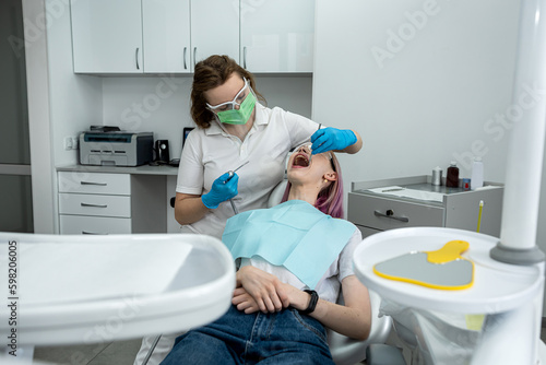 female dentist treats the teeth of a young girl patient lying in the clinic.
