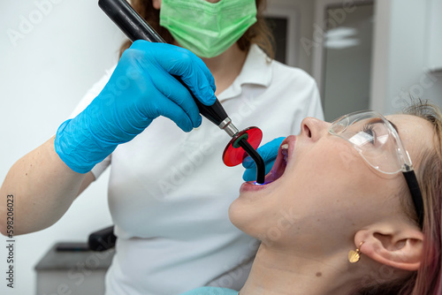 doctor dentist woman fixes a filling with the help of a UV lamp to a beautiful patient.