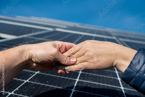 two pairs of hands shaking hands after making a deal on the background of solar panels. © RomanR