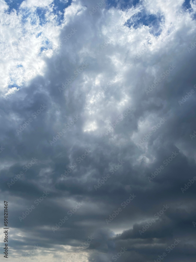The sky covered with dark clouds, close-up, view from below. A piece of blue sky is visible from behind the clouds. Cloudy cool spring day. Clouds of the lower tier. Cumuluses.