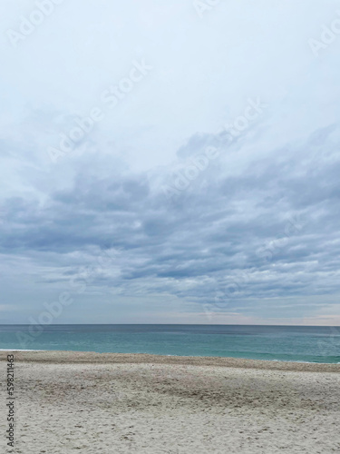 Seascape. Turquoise sea  blue sky with clouds and beige sandy shore  close-up  side view. Cloudy spring day. Beautiful view.