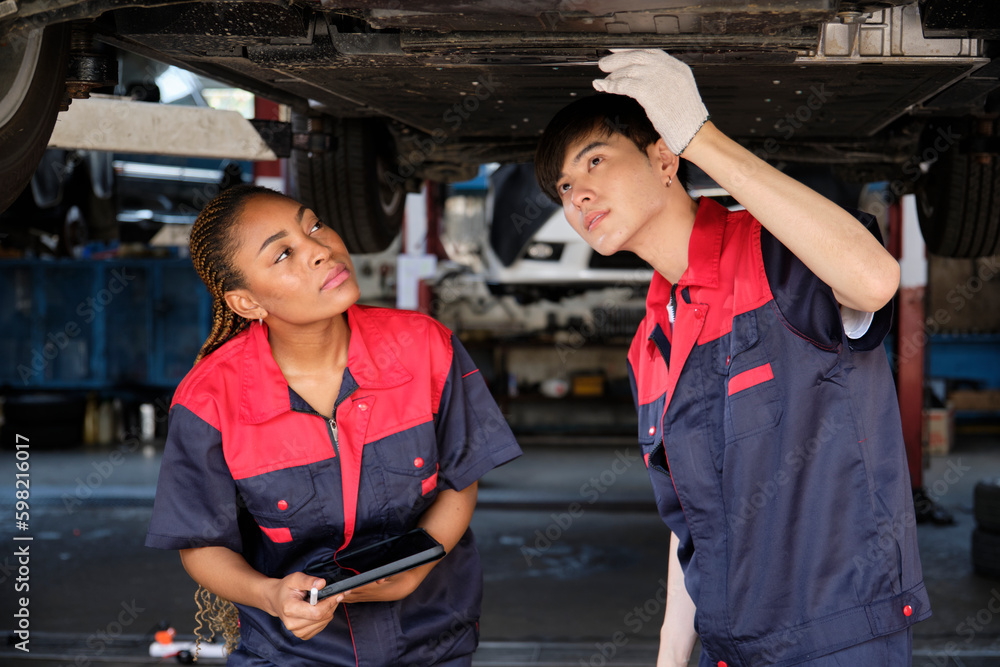 Two professional automotive worker partners discuss mechanical check undercarriage of lifted electric car, fix and repair at maintenance garage, and expert service business works industry occupation. Two professional automotive worker partners discuss mechanical check undercarriage of lifted electric car, fix and repair at maintenance garage, and expert service business works industry occupation.