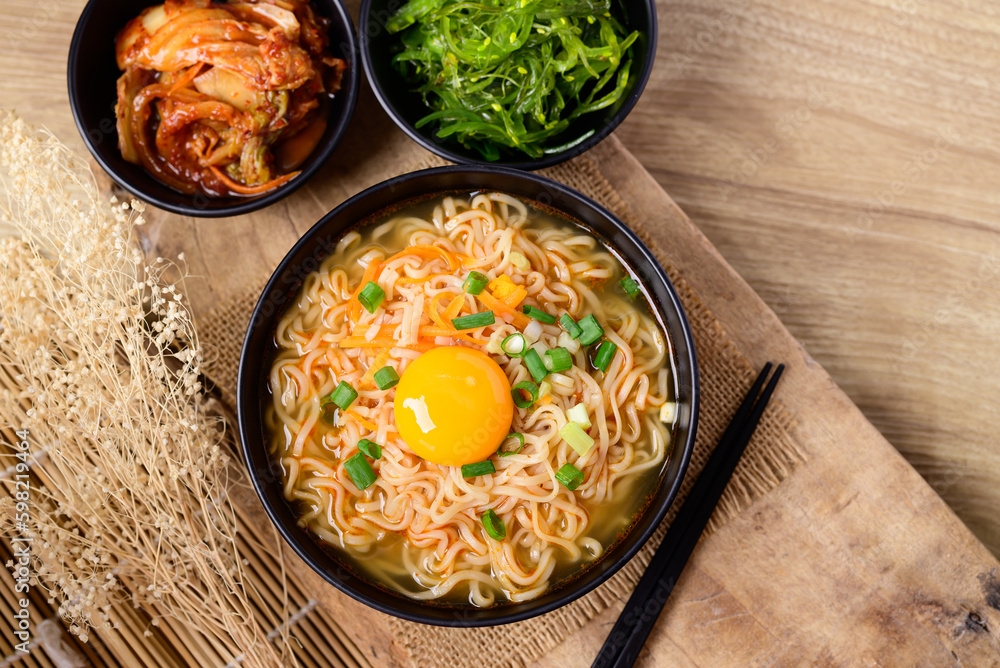 Asian instant noodle soup with fresh egg yolk eating with kimchi cabbage and seaweed salad, Table top view Asian instant noodle soup with fresh egg yolk eating with kimchi cabbage and seaweed salad, Table top view