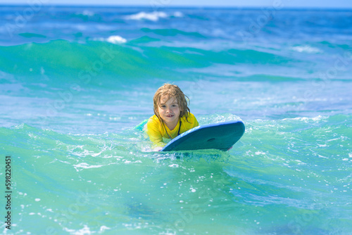 Kid little surfer learn to ride on surfboard on sea waves. Kids outdoor water sport, swimming activity in surf camp. Child summer vacation at sat. Kid learning to surf in sea or ocean. © Volodymyr