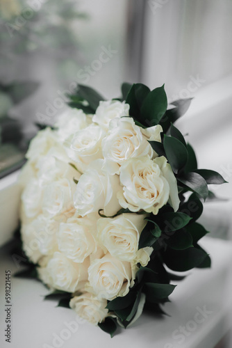 A bouquet of white roses and greenery on a white background. A beautiful photo with details of the wedding. Wedding day. Daylight.