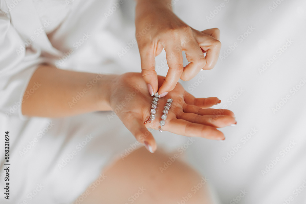 Photo of wedding details. The bride holds her silver diamond earrings. View from above. French manicure. Beautiful hands Photo of wedding details. The bride holds her silver diamond earrings. View from above. French manicure. Beautiful hands
