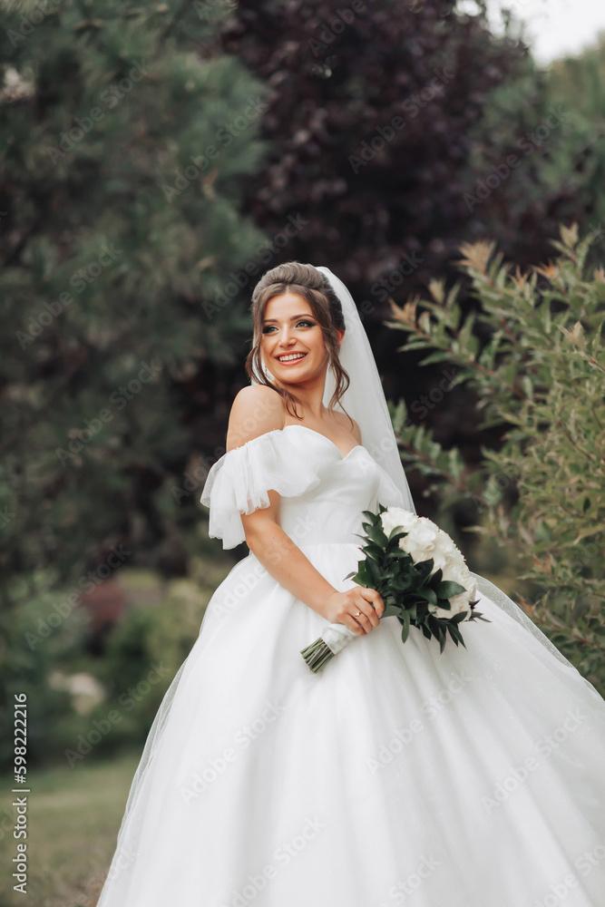 Wedding photo. The bride in a voluminous white dress and a long veil, smiling, twirling with a bouquet of white roses, holding her dress. Portrait of the bride. Beautiful makeup and hair. Wedding photo. The bride in a voluminous white dress and a long veil, smiling, twirling with a bouquet of white roses, holding her dress. Portrait of the bride. Beautiful makeup and hair.