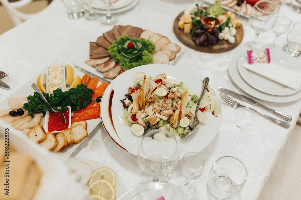 buffet table at a wedding. Cheese plate. Assortment of canaps. Banquet service. food, snacks with cheese, ham, prosciutto and fruit. Caesar salad. Glass glasses. Silver table sets. buffet table at a wedding. Cheese plate. Assortment of canaps. Banquet service. food, snacks with cheese, ham, prosciutto and fruit. Caesar salad. Glass glasses. Silver table sets.