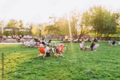 Fototapeta Naklejka Na Ścianę i Meble -  Blurred garden with lighting sunset. Public park with people. Blurred image of people in day in city park background
