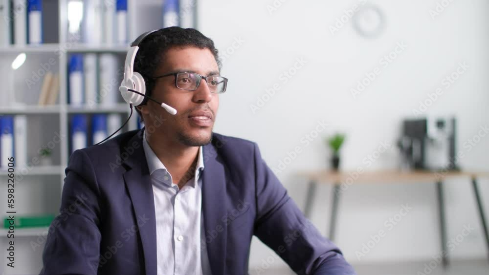 young attractive black man talking on a microphone on headphones with client working in support of a call center while sitting in office young attractive black man talking on a microphone on headphones with client working in support of a call center while sitting in office