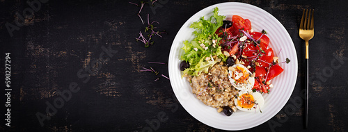 Breakfast oatmeal porridge with boiled egg, cherry tomatoes, olives, nuts and microgreens. Healthy balanced food. Top view, overhead