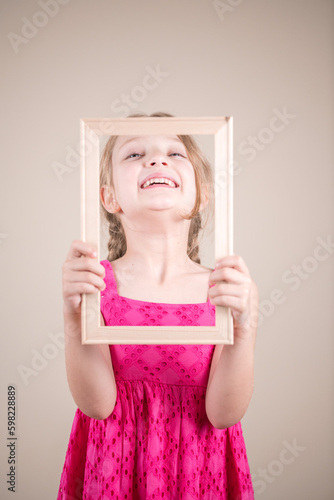 Little girl in a pink dress holding a picture frame.