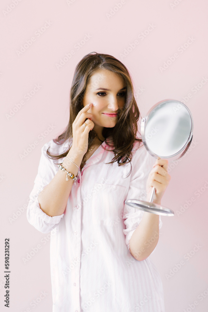 Young Caucasian woman puts cream on her face, looks in the mirror in the morning at home Young Caucasian woman puts cream on her face, looks in the mirror in the morning at home
