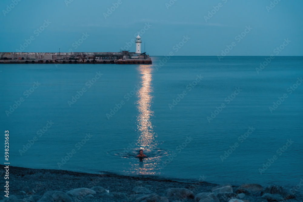Woman The full moon rises to the lighthouse, the lunar path along the sea leads to the woman.
