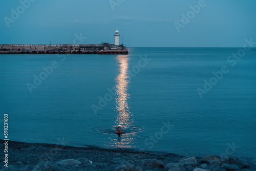 Woman The full moon rises to the lighthouse, the lunar path along the sea leads to the woman. © svetograph