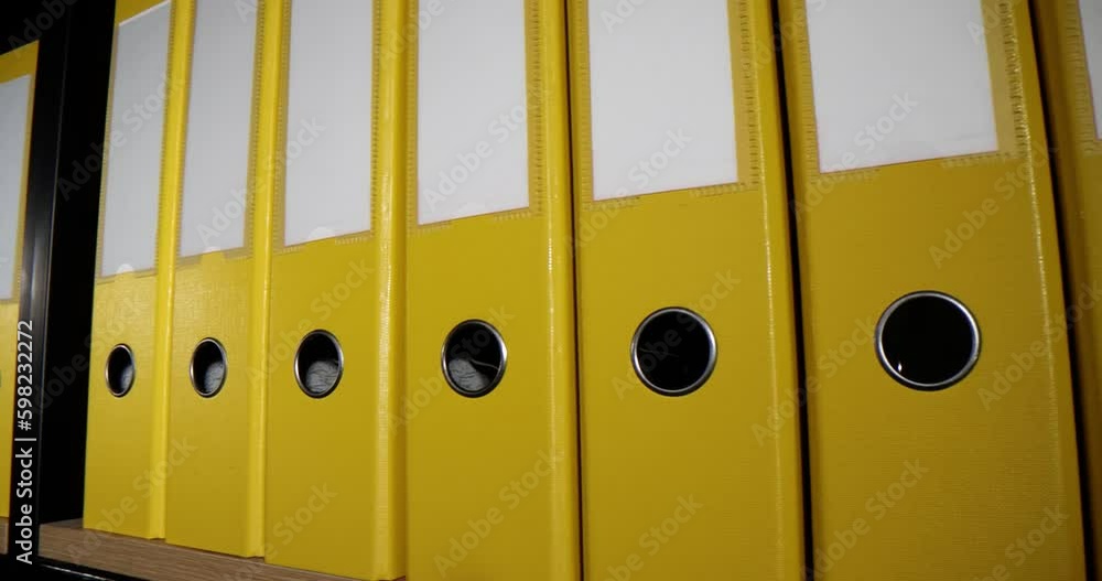 Yellow folders put in long line on shelf of rack in office premises. Organized structure of document ring binders with accounting materials and reports for work Yellow folders put in long line on shelf of rack in office premises. Organized structure of document ring binders with accounting materials and reports for work