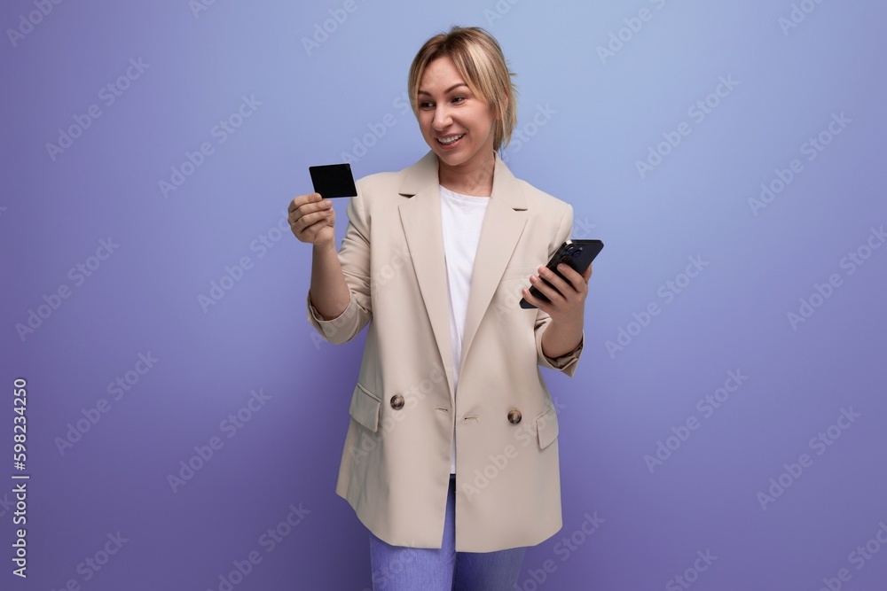 joyful blond woman pays for her purchases using a smartphone and an application with a bank on a studio background joyful blond woman pays for her purchases using a smartphone and an application with a bank on a studio background