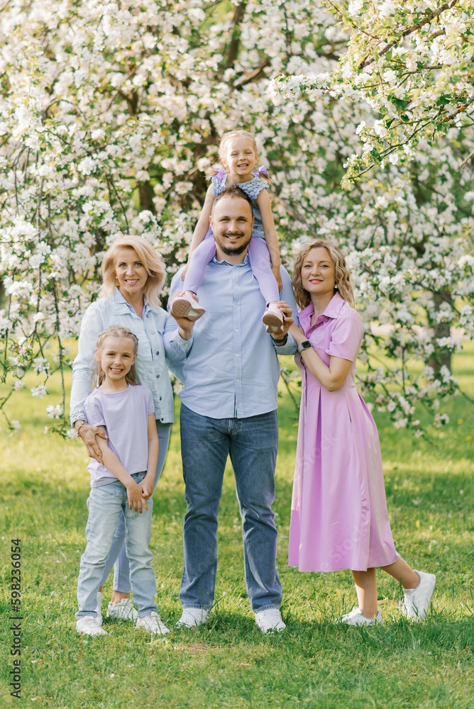 Portrait of a Caucasian family, parents, two daughters and a grandmother in a blooming spring garden