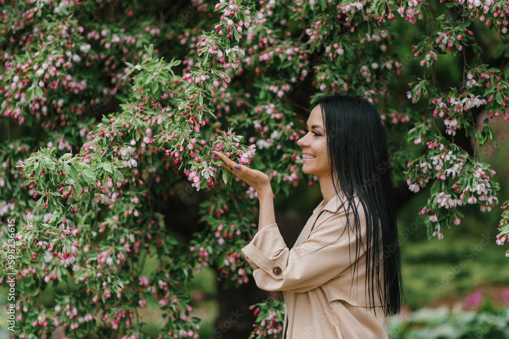 Caucasian young brunette woman sniffs the flowers of an ornamental apple tree in spring in the park Caucasian young brunette woman sniffs the flowers of an ornamental apple tree in spring in the park