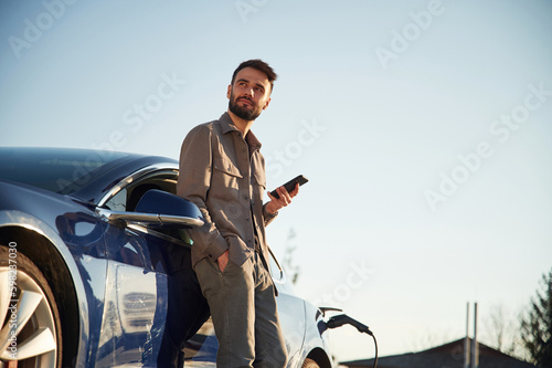 Man is standing near his electric car outdoors