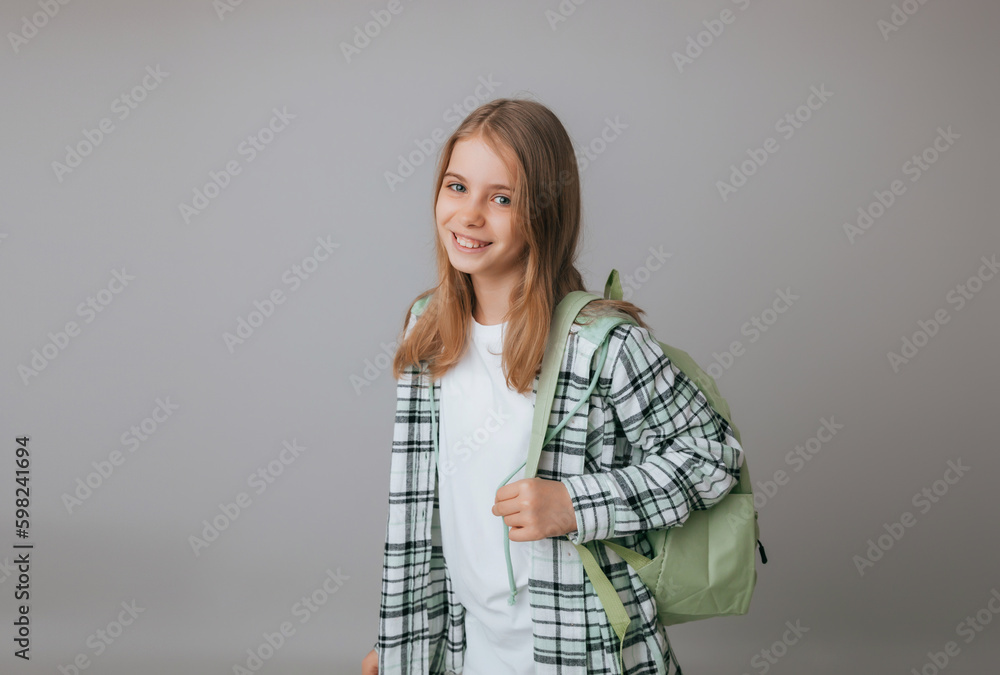 cheerful teenage girl 11,12,13 years old in a school uniform wears a backpack on a gray background. school fashion cheerful teenage girl 11,12,13 years old in a school uniform wears a backpack on a gray background. school fashion