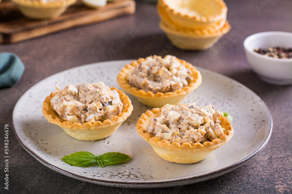 Appetizing tartlets with egg, canned tuna and onion salad on a plate on the table