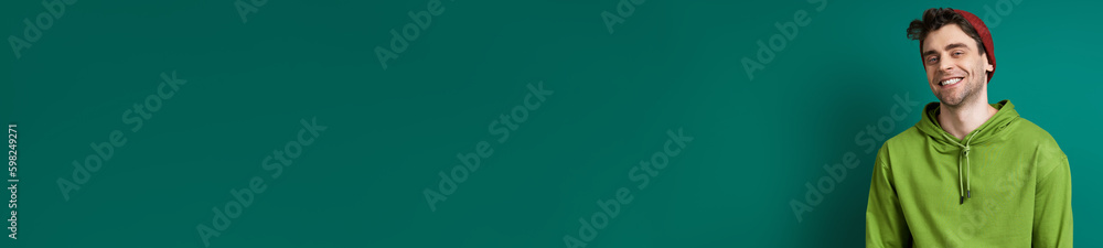 Stylish young man looking at camera and smiling while standing against green background Stylish young man looking at camera and smiling while standing against green background