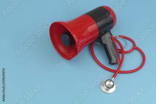 Red stethoscope and megaphone on blue background with copy space for text. Hire medical workers and call for medical help concept.