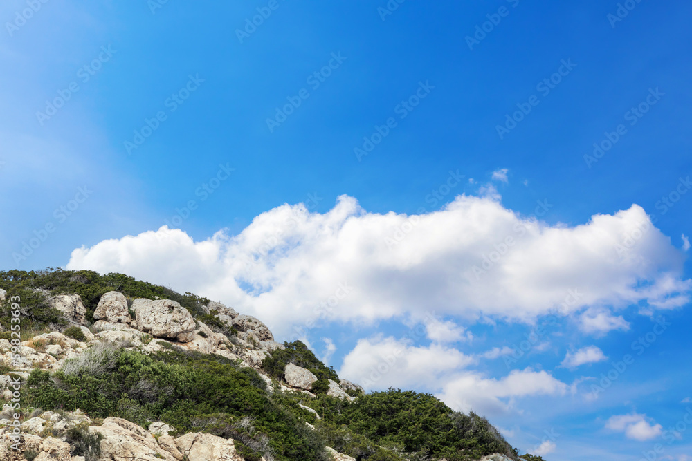 Close-up of a green rocky mountain peak, with a blue cloudy sky in the background. Nature view of mountain and sky with free space for text, copy space