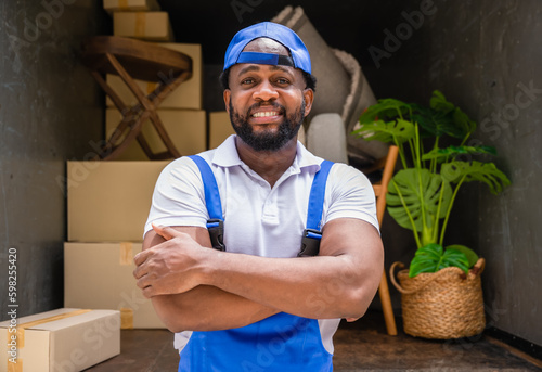 Portrait of happy African American delivery service man worker in uniform standing arms crossed and looking at camera with smiling outdoors with the truck background.