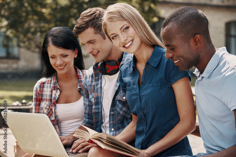 Group of young people using laptop and reading books while spending time outdoors together