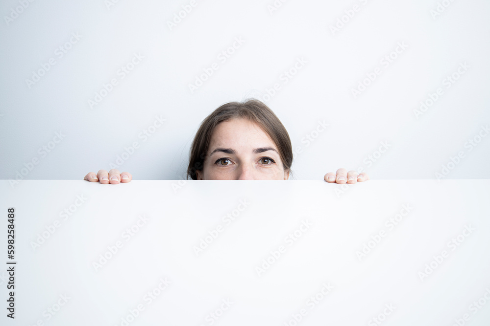 Young woman looking to the side looking out from under a white table against a white wall Young woman looking to the side looking out from under a white table against a white wall
