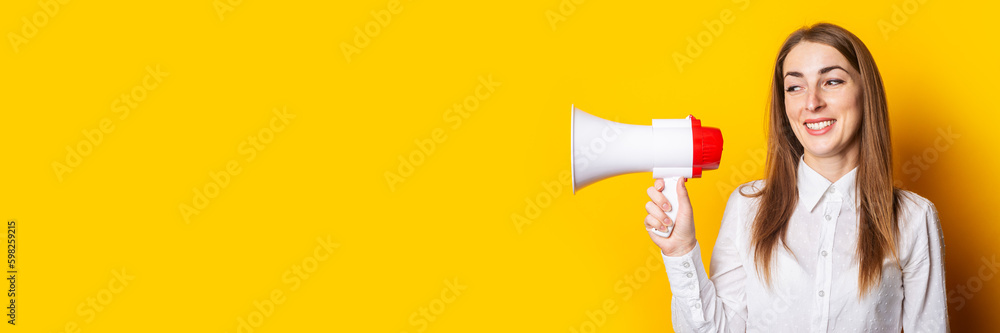 Friendly young woman holds a megaphone in her hands on a yellow background. Hiring concept, help wanted. Banner Friendly young woman holds a megaphone in her hands on a yellow background. Hiring concept, help wanted. Banner