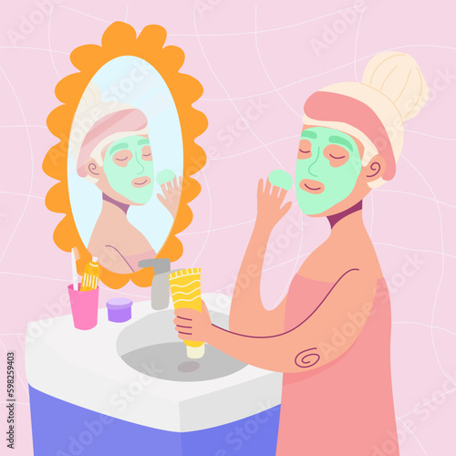 Woman  in the bathroom applying a face mask. Woman stands with cosmetics near mirror. Skincare routine.