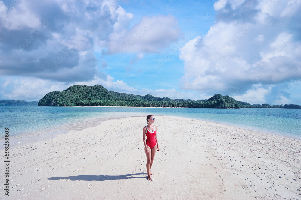 Vacation on the seashore. Young woman in red swimsuit walking on the beautiful tropical white sand beach.