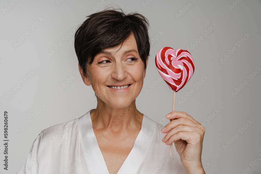 Smiling senior woman looking away while holding lollipop isolated over white background Smiling senior woman looking away while holding lollipop isolated over white background