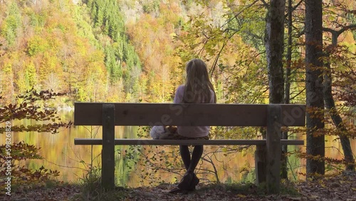 child girl sitting on the bench at the autumn park near the lake