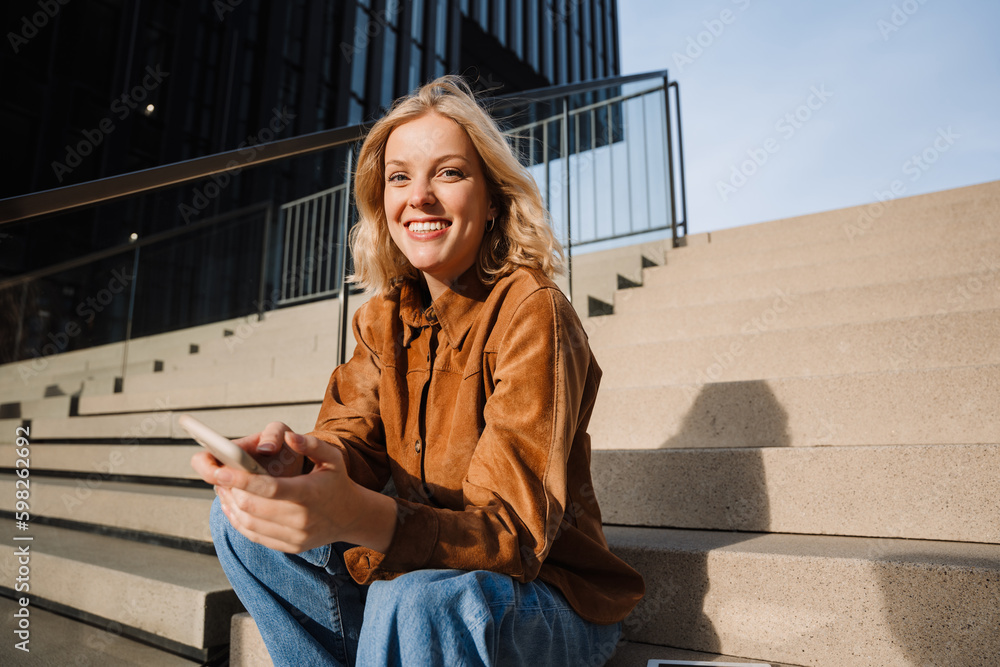 Smiling woman using smartphone while sitting on stairs outdoors Smiling woman using smartphone while sitting on stairs outdoors