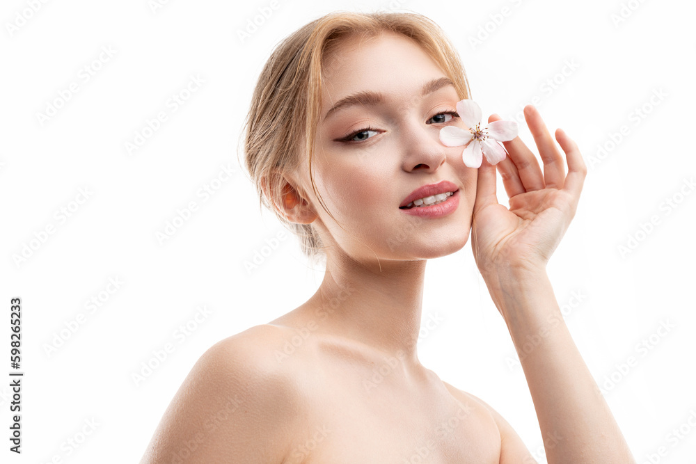 Beautiful girl with blond hair and pure soft skin with a flower looks at the camera Beautiful girl with blond hair and pure soft skin with a flower looks at the camera