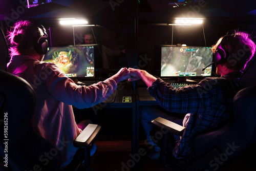 Fotografie, Obraz Two male gamers giving fist bump while playing video game together in cybersport